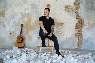 Young male with guitar in empty room, musician and songwriter alone in the studio