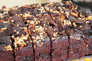Selected focused on the chocolate cake. Rectangular in shape. Crushed almonds are sprinkled on it. Has been cut into small cubes to make it easier to eat.