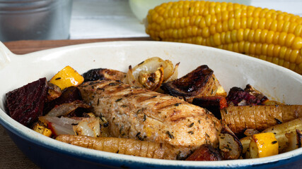 A grilled chicken is sitting in a ceramic plate alongside various root vegetables. The marks from the iron skillet is clearly visible as charred lines on the breast.
