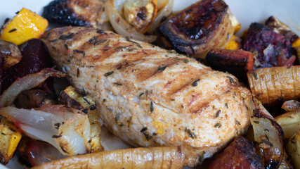 A grilled chicken is sitting in a ceramic plate alongside various root vegetables. The marks from the iron skillet is clearly visible as charred lines on the breast.