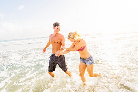 Young couple running in surf holding hands