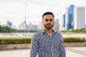 Young bearded Indian businessman relaxing at the park in the cit