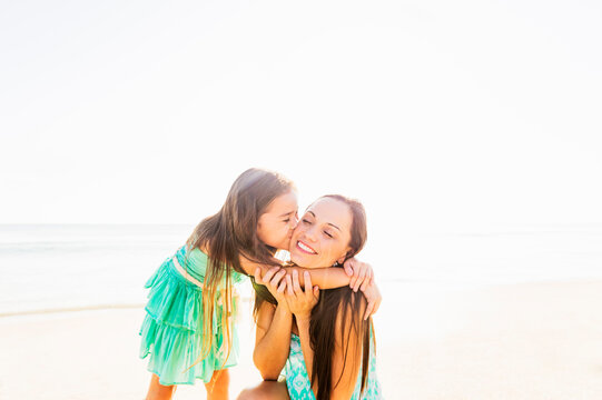 Girl (6-7) kissing her mother on cheek on beach