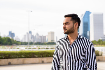 Young bearded Indian businessman relaxing at the park in the cit