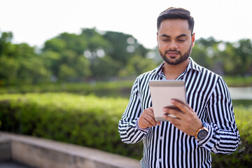 Young bearded Indian businessman relaxing at the park in the cit