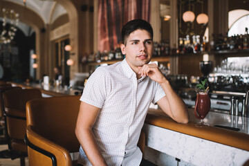 Young man relaxing in bar with drink leaning on bar counter