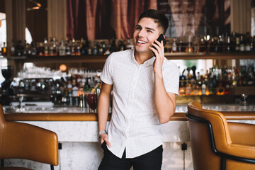 Happy man speaking on smartphone while standing at bar counter