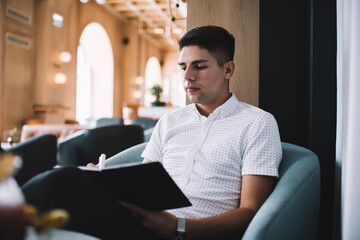 Thoughtful male author writing in agenda while sitting at cafe