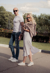 Fototapeta premium Stilish couple walking in modern clothers, white shoes and sunglasses on autumn city background in the park. Closeup