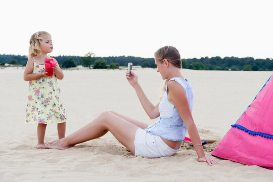 Mother taking picture of daughter (2-3) on beach