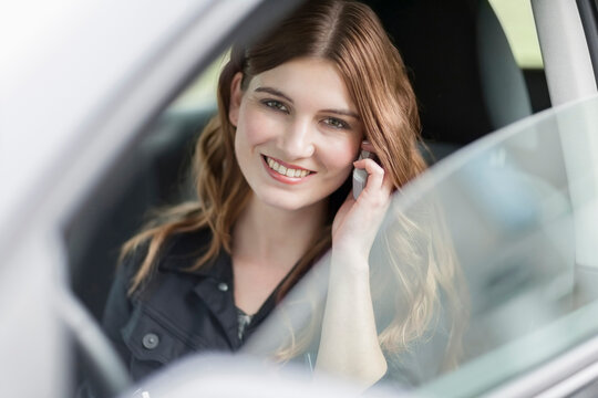 Young smiling woman speaking on phone in car