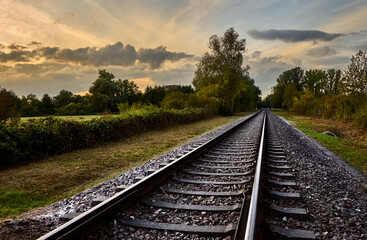 Fototapeta premium Train tracks through rural landscape against cloudy sky at sunset