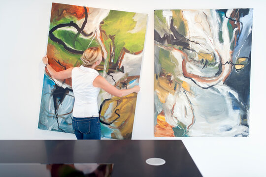 Woman hanging paintings indoors