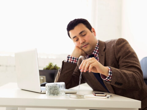 Businessman sitting in office and playing with paper clips