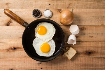 fried eggs, in a frying pan, on wooden background. Top wiew.