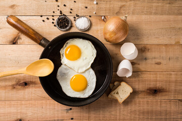 fried eggs, in a frying pan, on wooden background. Top wiew.