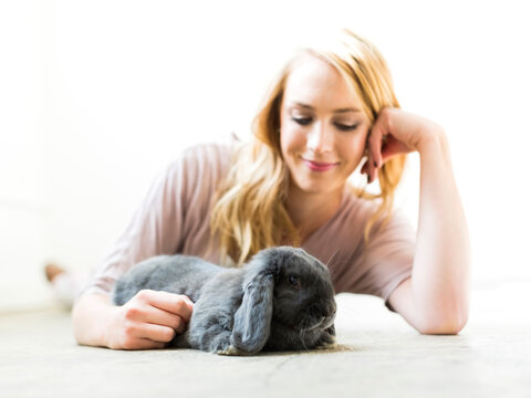 Young woman lying on floor and stroking rabbit