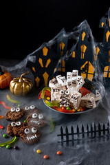 Modern Halloween background. Halloween candy bar: funny monsters made of biscuits with chocolate and ghosts marshmallow close-up on the table. Halloween party decoration. Trick or treat concept.