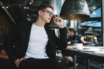 Thoughtful young man in eyeglasses sitting in cafe