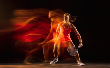 High jump. Professional female tennis player training isolated on black studio background in mixed light. Woman in sportsuit practicing. Healthy lifestyle, sport, workout, motion and action concept.