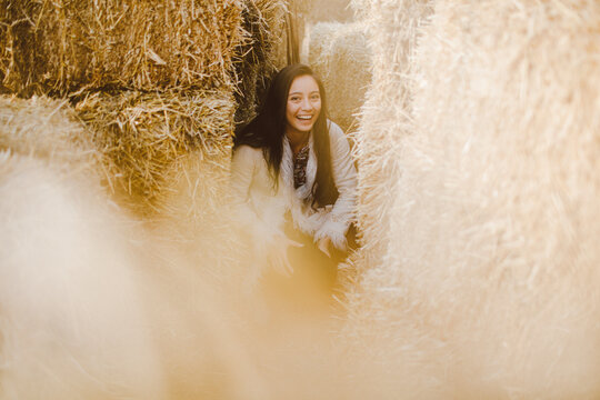 Laughing brunette girl sitting among hay stacks on a farm