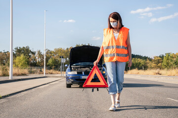 Woman with broken down car placing emergency triangle