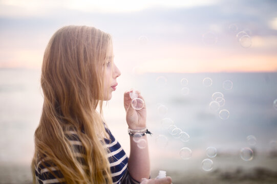 Girl blowing bubbles at the beach at sunset