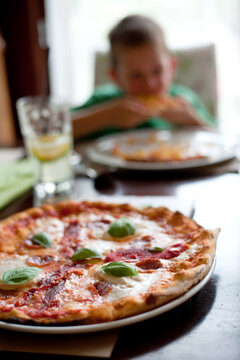 Italian style Margherita pizza on a table with a little boy in the background