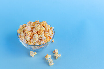 A transparent bowl of popcorn on a blue surface. Home family watching movies.