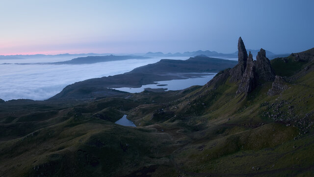 Atmospheric mysterious top view of the high sharp cliffs towering over the lakes and the sea covered with low clouds before dawn. The Old Man of Storr, The Isle of Skye, Scotland, UK.