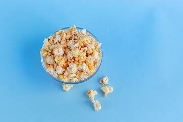 A transparent bowl of popcorn on a blue surface. Home family watching movies.