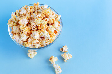 A transparent bowl of popcorn on a blue surface. Home family watching movies.