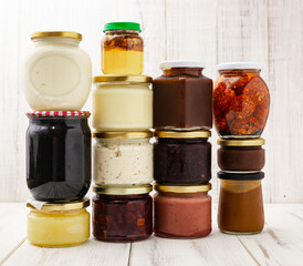 Various jars with canned vegetables, oils on a light wooden background.