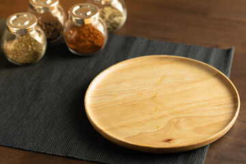 Empty wood tray or dish on black cloth placemat and a group of herbs and spices in jars on a conners