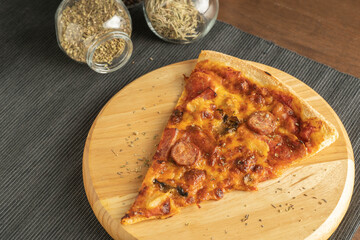 Close up on a pizza with pepperoni topping on a rounded wood tray place on black cloth placemat and a group of herbs and spices in jars on a conners