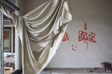 A torn curtain flails in the wind over a broken window at an abandoned hospital in Japan