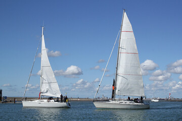 two beautiful white sailboats are sailing in the in the sea at the dutch coast in Breskens during an ocean race in summer and a blue sky