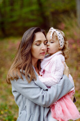 Fototapeta premium Mother holds daughter in her arms in the park on a sunny day. Autumn day.