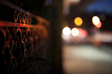 A wrought-iron fence at night with blurred traffic in the background.