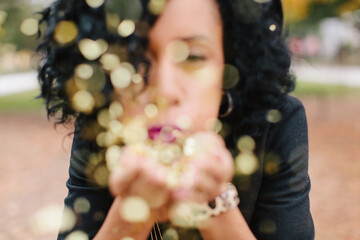 Young woman blowing gold glitter from her hands.