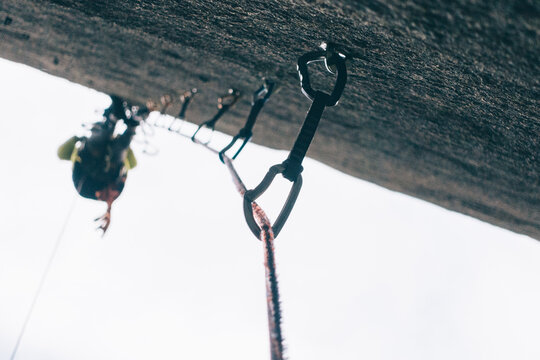 Mountaineer rock climbing a wall with the view of all the climbing quickdraws below him