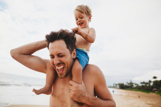 Young dad having fun with toddler son on tropical beach - kid pulling hair