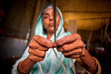 An old age woman is making on his skinny hands a rope from the banana tree fiber at Madhupur,...