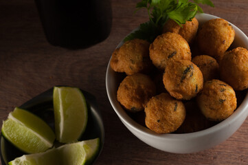 Salt cod fritters in a white bowl with chopped lemons and olive oil bottle. Selective focus