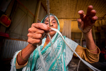 An old age woman is making on his skinny hands a rope from the banana tree fiber at Madhupur, Tangail, Bangladesh.