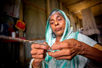 An old age woman is making on his skinny hands a rope from the banana tree fiber at Madhupur,...