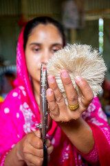 A woman making handicrafts is smoothing the fibers of a banana tree with scissors in Madhupur,...