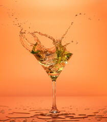 Vermouth cocktail splashing out of a martini glass isolated on orange backdrop