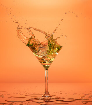 Vermouth cocktail splashing out of a martini glass isolated on orange backdrop