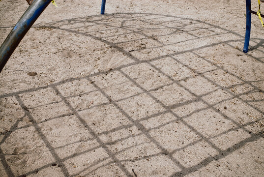 Shadows Of A Jungle Gym On The Sand Below.